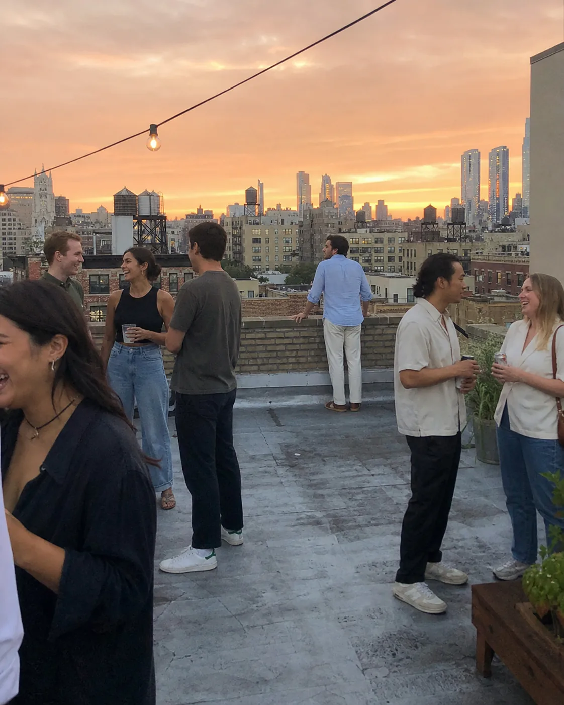 Alex looking over the city while friends talk on a rooftop